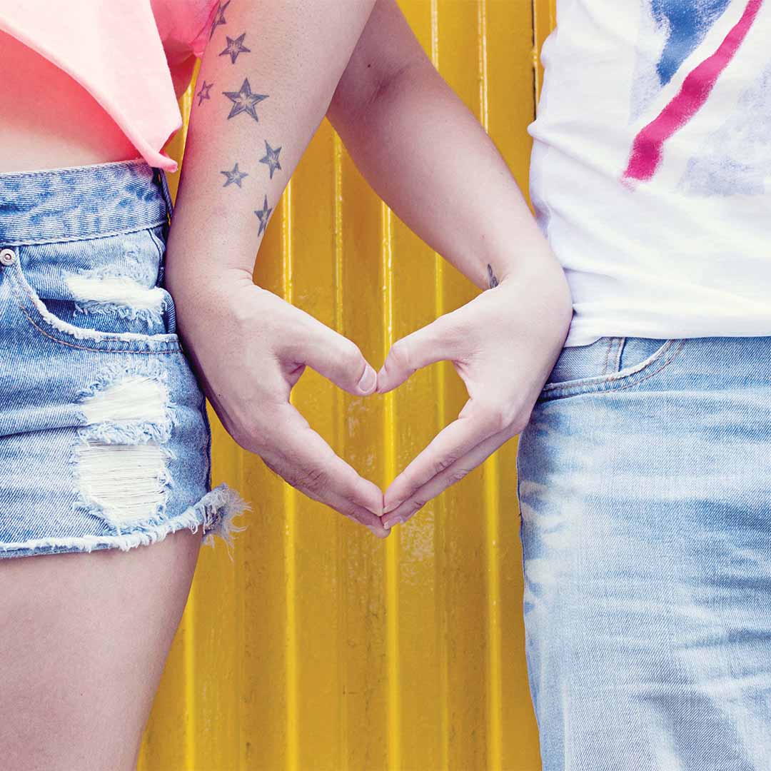 A male and female couple making a heart shape with their hands with star tattoos going down the guys arm and wrist