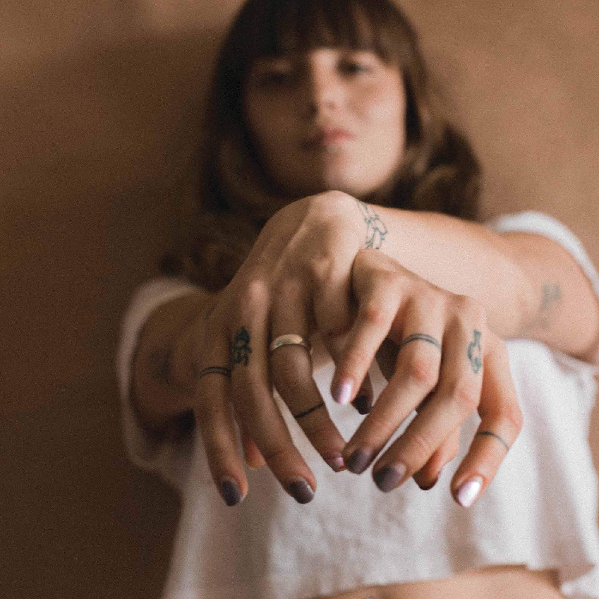 A women with her crossed over hands in front of her with tattoos on her hands and fingers.  