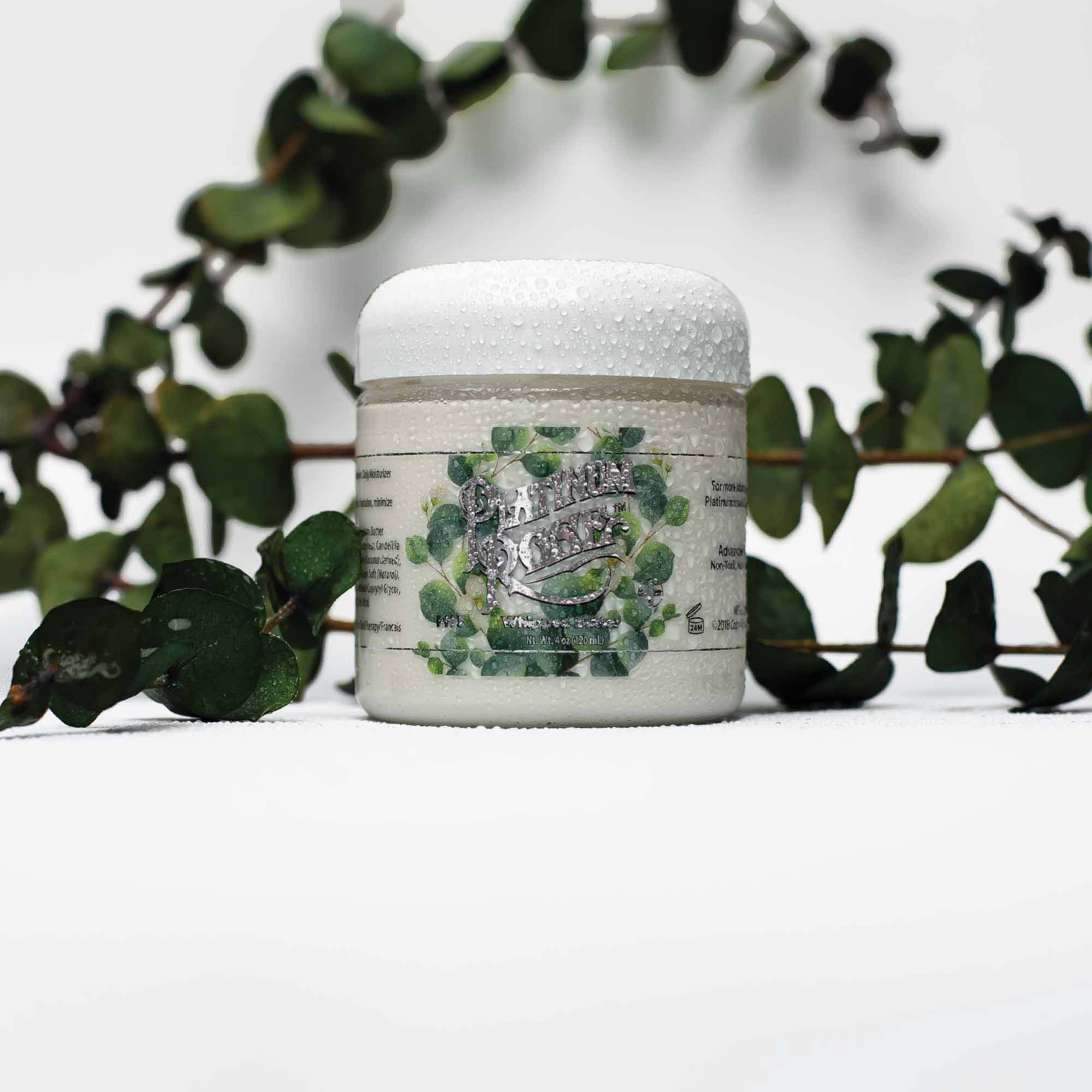 2oz jar of Platinum Rose tattoo Aftercare eucalyptus whipped butter surrounded by freshly cut eucalyptus leaves.