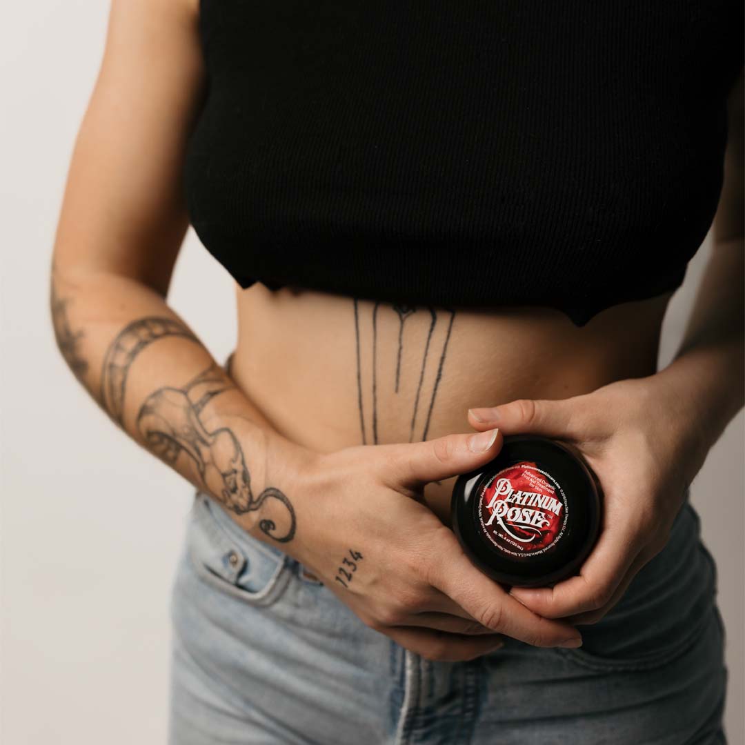 A women with minimalistic styled tattoos holding a 4oz jar of Platinum Rose Tattoo Aftercare 